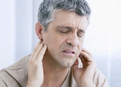 Man holding jaw in pain before diagnosis and T M J treatment