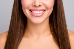 Nose-to-chest closeup of a woman with long brown hair smiling with perfectly straight teeth